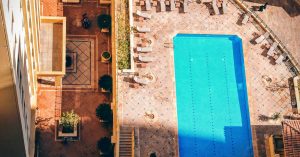 Aerial view of a luxurious hotel pool with sunlit surrounding seating and patio.