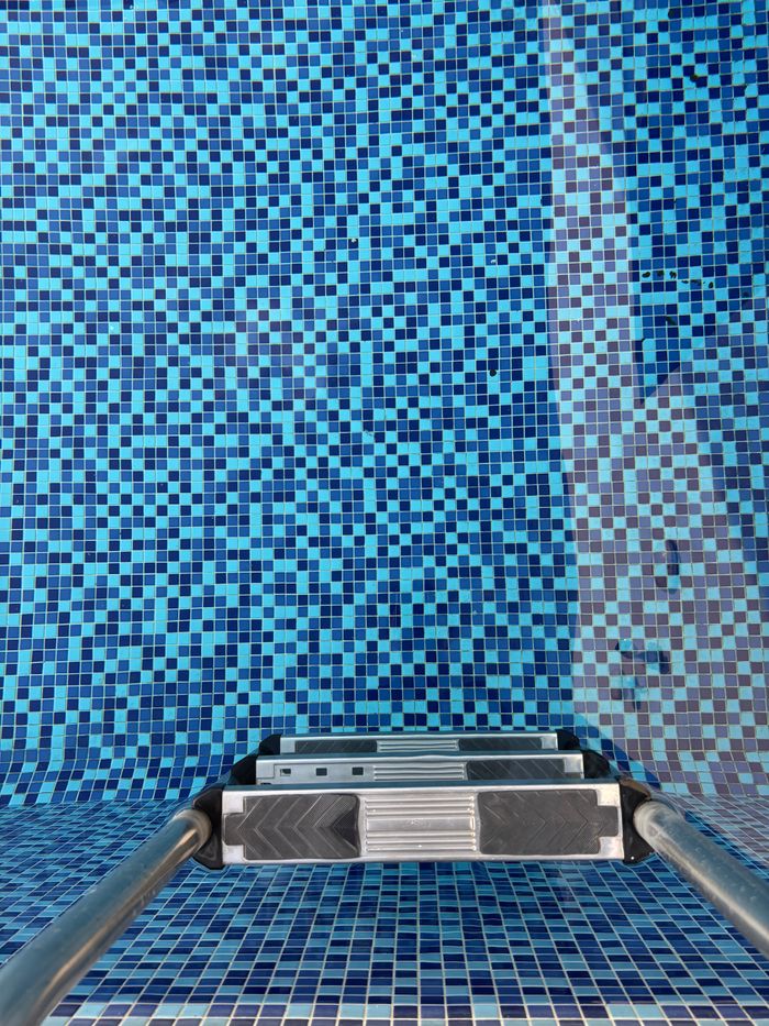 A dynamic perspective of a swimming pool featuring a vibrant blue mosaic tile pattern with ladder.