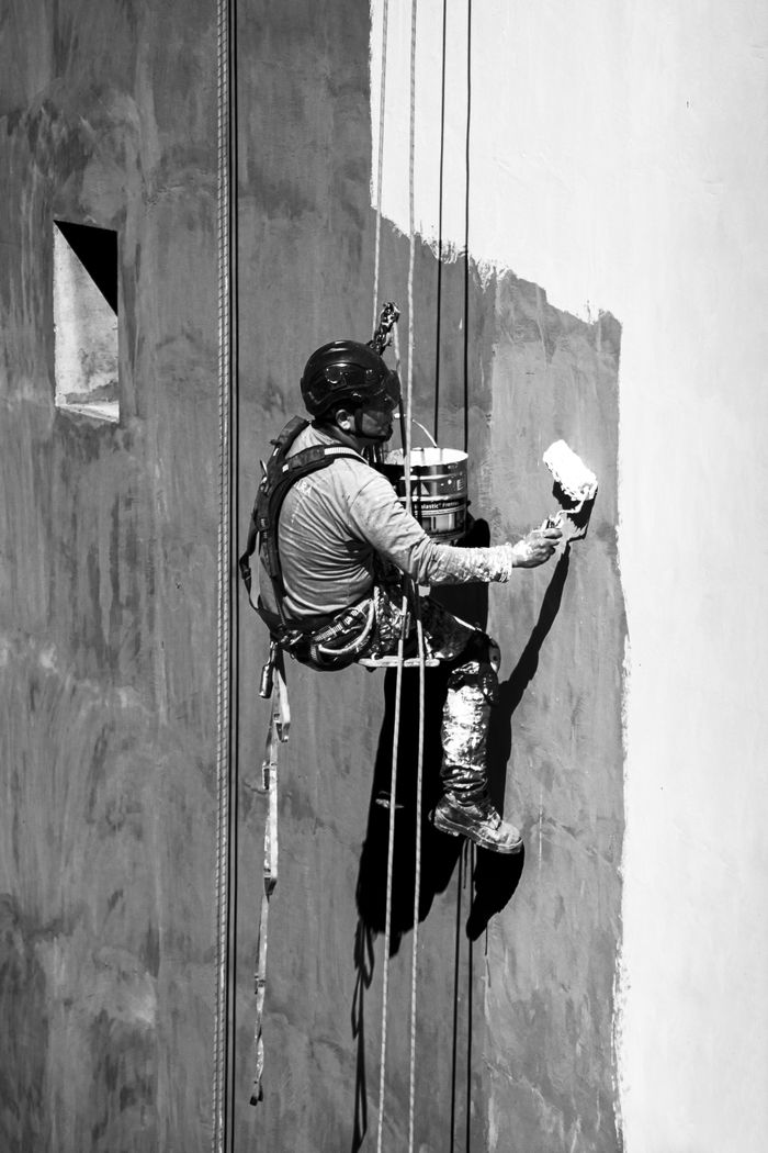 Man suspended on ropes painting a high-rise building wall in Buenos Aires.