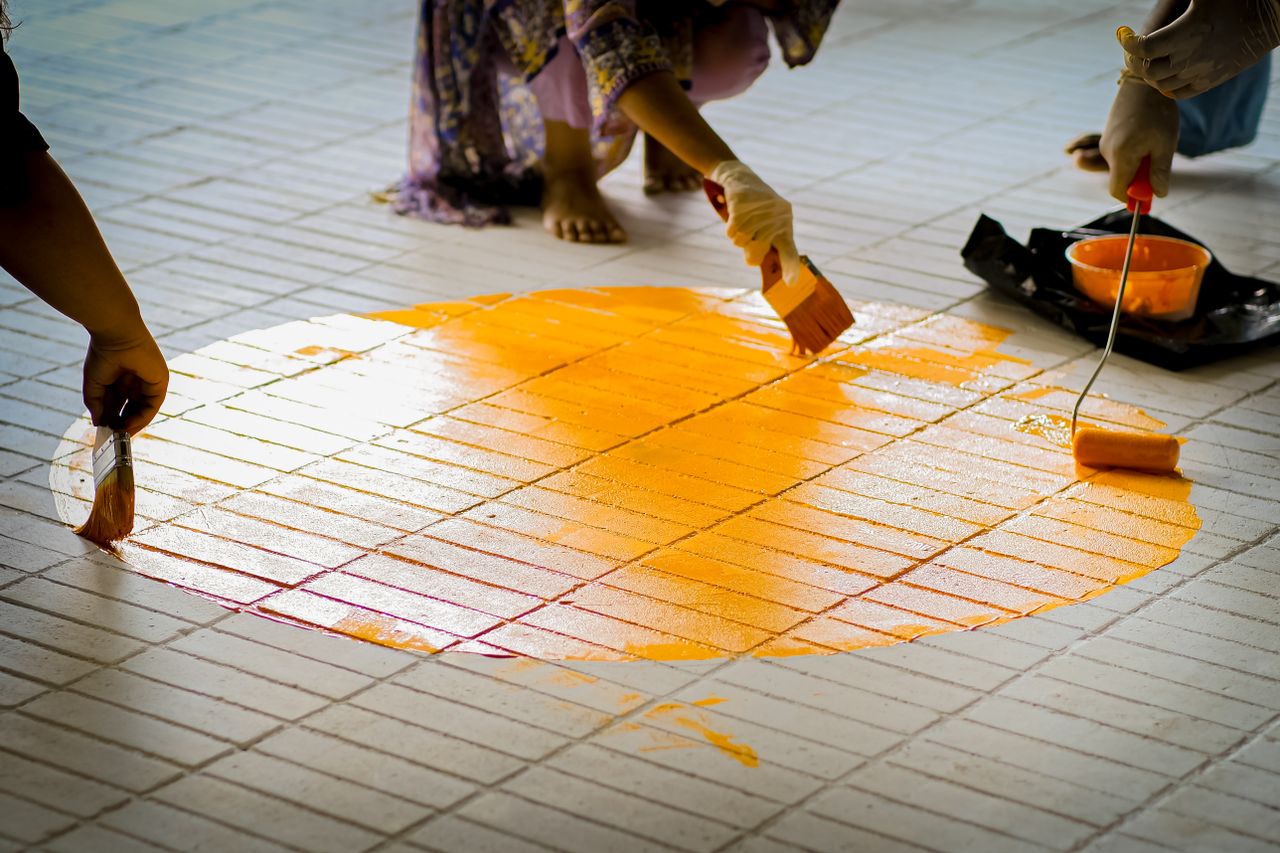 Group of people painting a vibrant orange circle on a tiled floor.